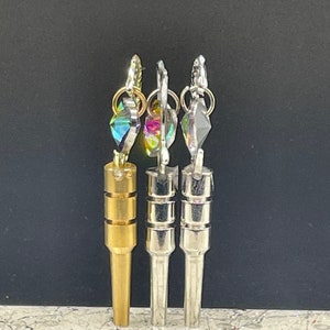 May include: Three metal keychains with different colored crystal charms. The keychain on the left is gold, the middle keychain is silver, and the keychain on the right is silver.