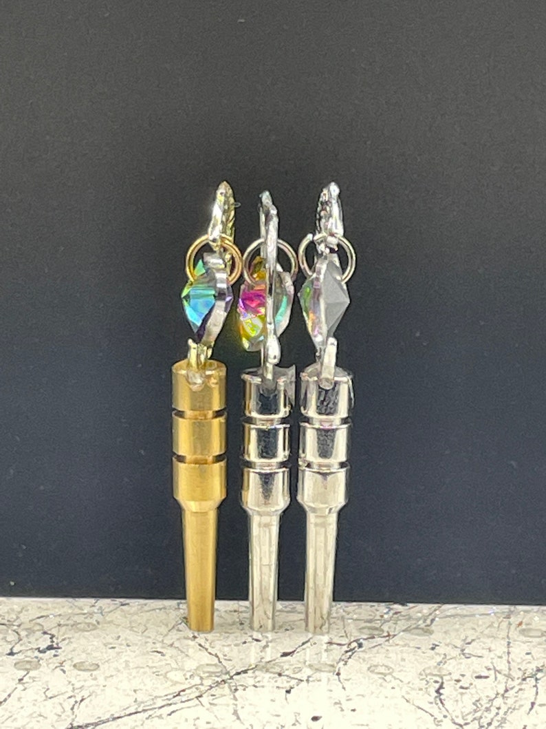 May include: Three metal keychains with different colored crystal charms. The keychain on the left is gold, the middle keychain is silver, and the keychain on the right is silver.