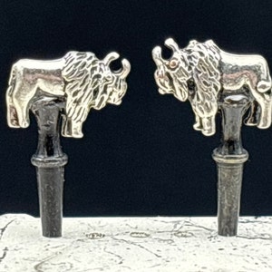 May include: Two silver buffalo head bottle stoppers with black wooden bases.
