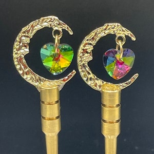 May include: A pair of gold-tone earrings with a crescent moon design and a dangling heart-shaped crystal. The crystals are iridescent and have a rainbow of colors.