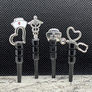 May include: Five silver medical themed charms on black posts. The charms include a nurse's hat with a heart, a caduceus, a first aid kit, a heart, and a stethoscope.