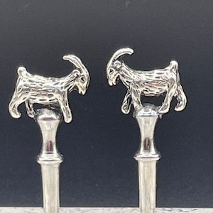 May include: Two silver goat bottle stoppers with detailed carvings. Each stopper features a goat standing on a cylindrical base.