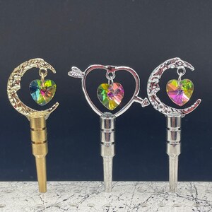 May include: Three silver and gold keychains with a crescent moon, heart, and arrow design. Each keychain features a colorful iridescent crystal heart charm.