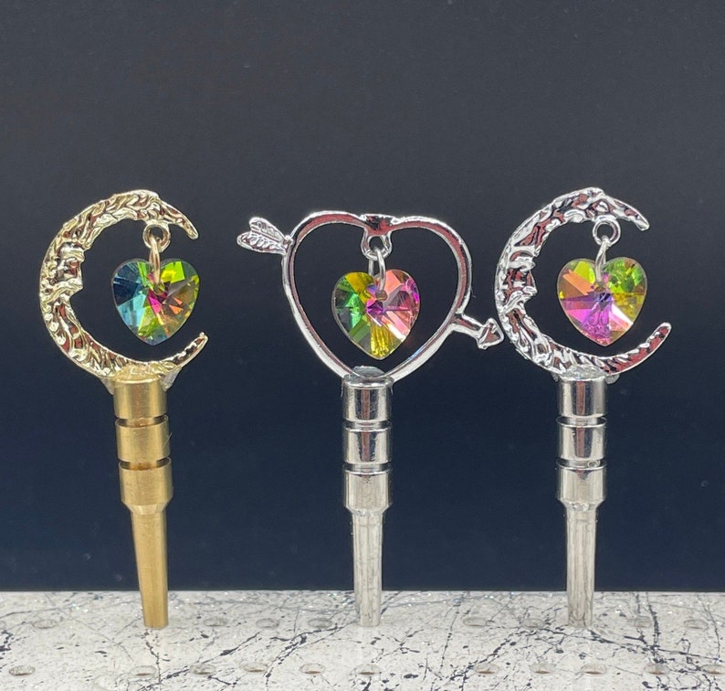 May include: Three silver and gold keychains with a crescent moon, heart, and arrow design. Each keychain features a colorful iridescent crystal heart charm.