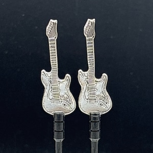 May include: Two silver-colored guitar-shaped earphone jack plugs. The plugs have detailed designs of electric guitars, including the body, neck, and strings. The background is a dark, solid color.