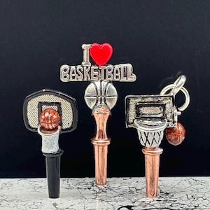 May include: Three basketball-themed keychains. One features a black backboard and a basketball in the net. Another has the text "I ❤️ BASKETBALL" with a red heart. The third has a silver backboard and a basketball.