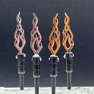 May include: Four black dart shafts with flame-shaped metal tips. The tips are in different colors: pink, copper, gold, and orange.