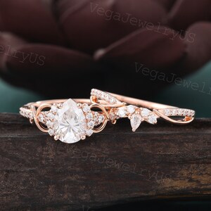 Puede incluir: Un anillo de compromiso de diamante de forma pera engastado en oro rosa con una banda delicada. El anillo presenta un halo de diamantes más pequeños y una banda retorcida. La banda de boda a juego es una banda simple con pequeños diamantes.