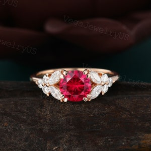 May include: A rose gold engagement ring with a large, round, red ruby gemstone surrounded by smaller, pear-shaped, white diamonds.
