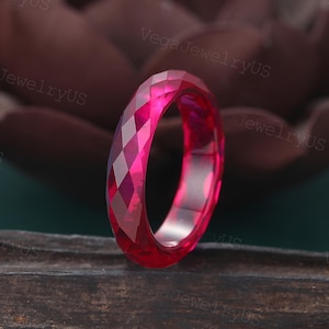 Puede incluir: Un anillo facetado de color rosa brillante. La superficie del anillo está cortada con múltiples facetas, creando un patrón geométrico. El anillo es de un tono rosa vibrante, y la luz atrapa las facetas, creando un efecto brillante. El anillo es de estilo banda.