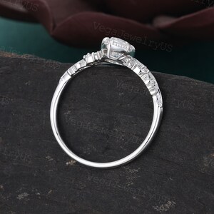 May include: A silver engagement ring with a round centre stone and smaller stones on the band. The ring is set on a dark green surface.