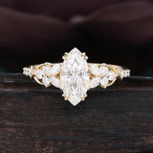 May include: A gold ring featuring a large marquise-cut center stone flanked by two clusters of three smaller marquise-cut stones on each side. The band is crafted from polished yellow gold, showcasing a delicate, intertwined metal design.