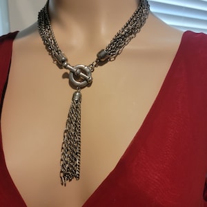 May include: A silver multi-strand necklace with a large, silver, toggle clasp and a tassel pendant.