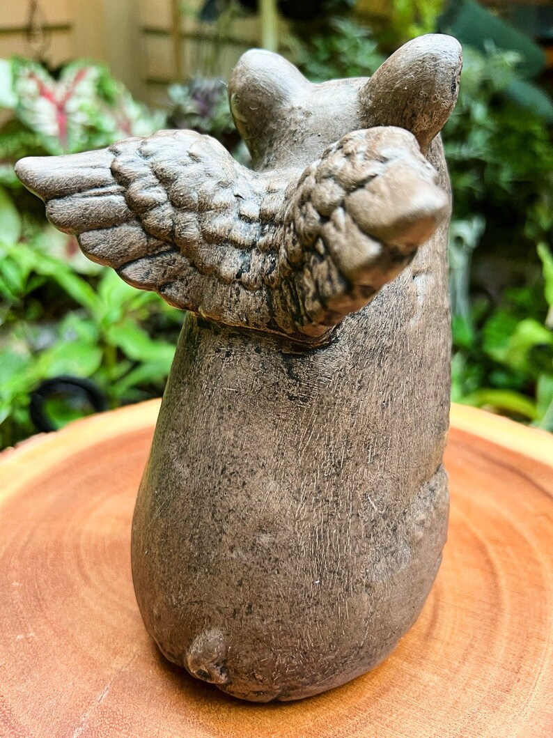 May include: A small, brown, ceramic figurine of a pig with wings. The pig is sitting on its hind legs with its wings spread out behind it.