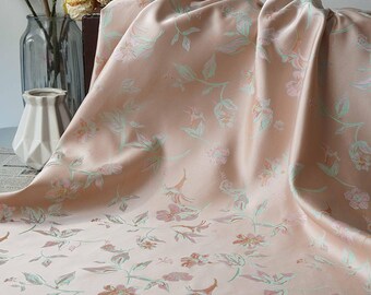May include: A draped, peach-colored fabric with a floral pattern in shades of pink and green. The fabric has a silky sheen, suggesting a satin or silk material. The floral design features stylized flowers and leaves.