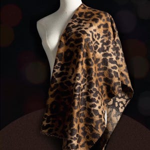 May include: A leopard print fabric draped over a mannequin. The fabric has a brown and black spotted pattern. The word "FASHION" is visible in the background. The fabric is likely used for clothing or accessories.