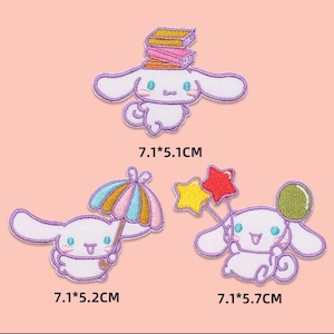 Pode incluir: Conjunto de três patches bordados com um personagem de desenho animado branco com orelhas compridas. Um patch tem livros na cabeça, outro segura um guarda-chuva e o terceiro varinhas de estrelas e um balão. Medem aproximadamente 7,1 x 5,1 cm, 7,1 x 5,2 cm e 7,1 x 5,7 cm.