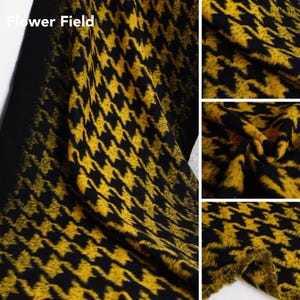 Puede incluir: Tela de pata de gallo negra y amarilla con el texto "Flower Field". La tela presenta un patrón repetitivo de formas amarillas sobre un fondo negro. La tela está doblada y drapeada, mostrando su textura.
