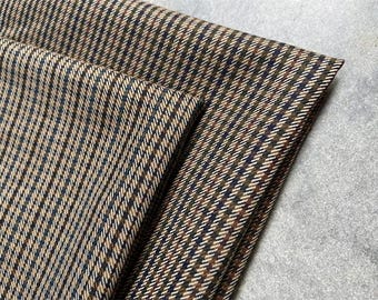 Puede incluir: Primer plano de tela doblada con un patrón de espiga marrón, azul marino y blanco. La tela está tejida apretadamente, con un diseño diagonal. La textura parece suave y adecuada para proyectos de ropa o decoración del hogar.