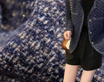 May include: A navy blue tweed jacket with gold trim and buttons. The jacket has a classic design and is paired with black shorts. The tweed fabric has a textured appearance with flecks of gold.