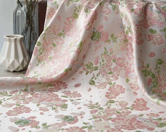 May include: A flowing fabric with a floral pattern in shades of pink and green on a white background. The fabric is draped, showcasing the intricate design of the flowers and leaves. The overall aesthetic is soft and elegant.