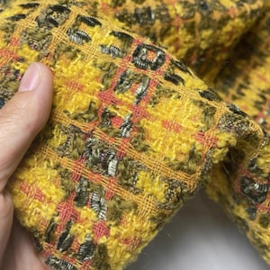 Puede incluir: Primer plano de una tela texturizada con un patrón de cuadros amarillos, marrones y rojos. La tela tiene un aspecto tejido con una textura ligeramente elevada. Los colores son vibrantes y el tejido es intrincado.