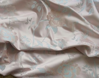May include: Pale pink fabric with a delicate floral pattern in shades of blue and pink. The fabric has a subtle sheen and a soft, luxurious feel.