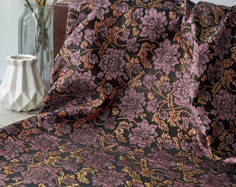 May include: A draped fabric with a floral pattern. The fabric features large, stylized flowers in shades of purple and gold against a black background. The design includes intricate details and a textured appearance, suitable for upholstery or decorative projects.