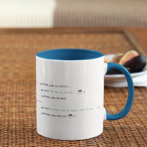 Op de afbeelding: Een witte keramische mok met een blauwe binnenkant en handvat, voorzien van zwarte programmeercode met de tekst: if coffee_cup.is_full(): print("Drinking coffee..."), coffee_cup.drink(), else: print("Coffee cup is empty. Refilling..."), coffee_cup.refill().