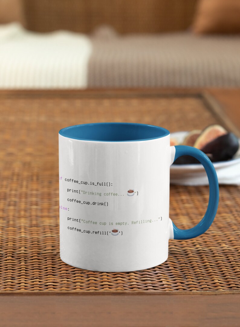 Op de afbeelding: Een witte keramische mok met een blauwe binnenkant en handvat, voorzien van zwarte programmeercode met de tekst: if coffee_cup.is_full(): print("Drinking coffee..."), coffee_cup.drink(), else: print("Coffee cup is empty. Refilling..."), coffee_cup.refill().
