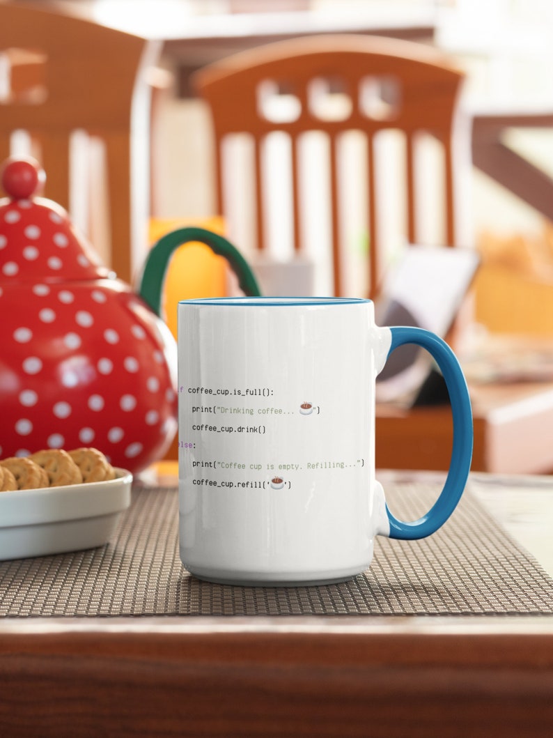 Op de afbeelding: Een witte keramische mok met een blauwe binnenkant en handvat, voorzien van zwarte programmeercode tekst die luidt: if coffee_cup.is_full(): print("Drinking coffee... ☕") coffee_cup.drink() else: print("Coffee cup is empty. Refilling...") coffee_cup.refill('☕')