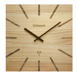 Op de afbeelding: Vierkante houten klok met het woord "Holzwerk" op de wijzerplaat. De klok heeft donkerbruine wijzers en een draadloos symbool. De wijzerplaat heeft een licht houtnerfpatroon en donkerbruine lijnen die de uren markeren.