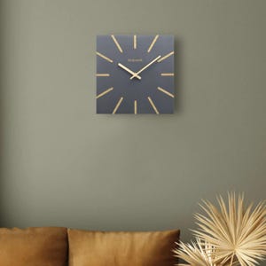 Holzwerk MAINBURG eckige Holz Wanduhr 25 cm Ø moderne analoge quadratische Wand Uhr, nahezu lautloses Uhrwerk, grau, beige, hängend an einer Oliven grünen flachen Wand