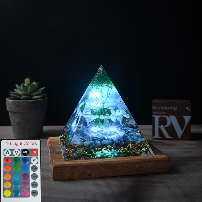 May include: A pyramid-shaped resin lamp with a wooden base. The lamp is lit with a blue and white light and contains various crystals and stones. The lamp has a remote control with 16 light colors. The remote control has buttons for on, off, red, green, blue, white, flash, fade, and smooth.