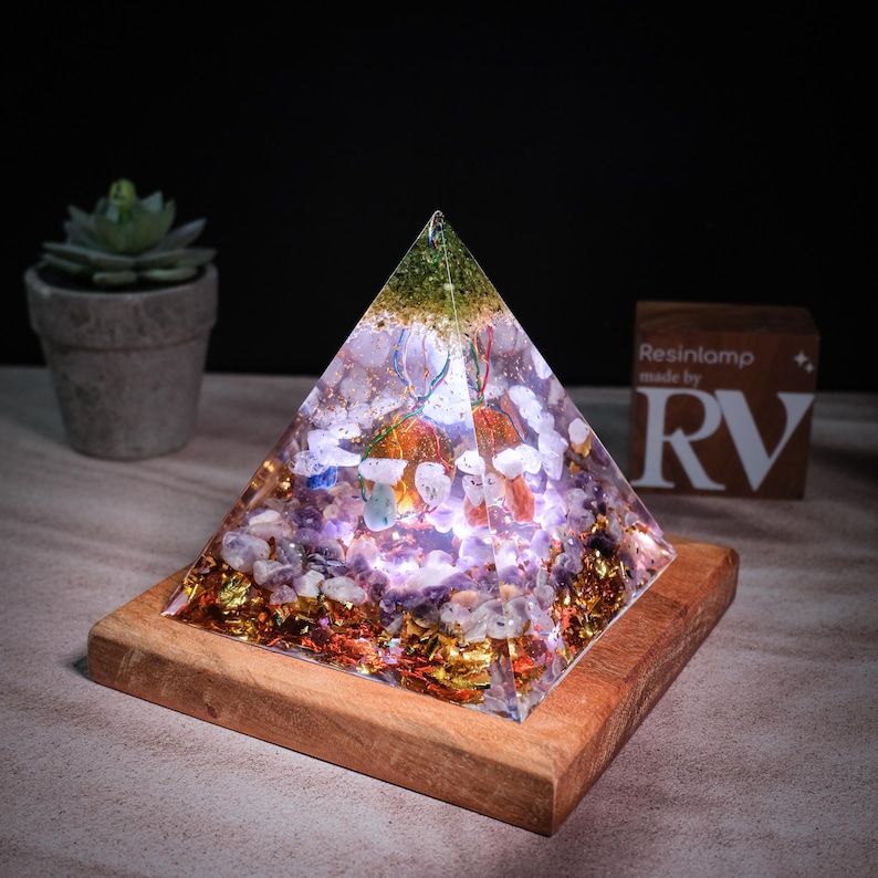 May include: A clear resin pyramid with a variety of crystals and gold flakes inside. The pyramid is lit from within, casting a warm glow. It is sitting on a wooden base. Resinlamp made by RV.