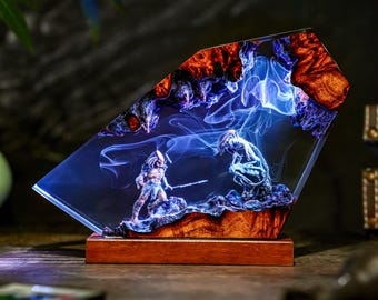 Op de afbeelding: Een hars sculptuur met twee Predator figuren in een gevechtsscène, ingekapseld in een helder, schuin blok. De sculptuur staat op een houten voet en wordt verlicht met blauwe en oranje tinten, wat een dramatisch effect creëert. De figuren zijn gedetailleerd en de hars heeft een rokerig uiterlijk.
