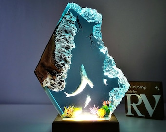 Könnte beinhalten: Eine Harzlampe mit einem blauen und weißen Wal-, Fisch- und Korallendesign. Die Lampe ist beleuchtet und strahlt ein warmes Licht aus. Die Lampe wird von RV Resinlamp hergestellt.