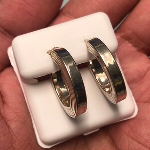 May include: A pair of silver hoop earrings. The earrings are presented on a white jewellery card. The hoops have a layered design, with a shiny, reflective surface. The earrings are a classic jewellery item.
