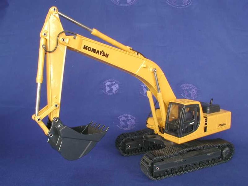 Puede incluir: Un modelo de juguete de excavadora Komatsu PC400-8 amarillo con orugas negras y una cuchara negra. La excavadora est&aacute; colocada con el brazo levantado y la cuchara extendida.