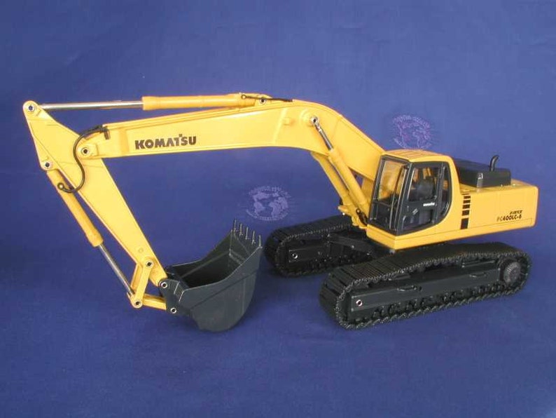 May include: A yellow Komatsu PC400LC-8 excavator toy model with black tracks and a black bucket. The model has a detailed cab with a clear window and the text "Komatsu PC400LC-8" on the side.