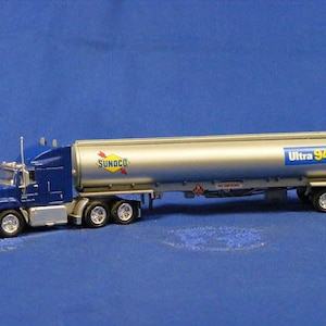 May include: A miniature blue and silver tanker truck, featuring the Sunoco logo and "Ultra 94 Octane" branding. The truck has a blue cab and a silver tank trailer, with six wheels. The model is set against a blue backdrop.