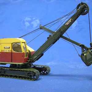 以下が含まれることがあります： 黒いケーブルシステムと緑のバケットが付いた、緑と黄色のBucyrus Erie 22-Bクローラークレーンの玩具モデルです。