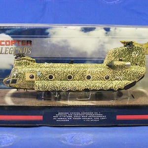 May include: A 1/72 scale model of a Boeing-Vertol Chinook HC.1 helicopter in a desert camouflage paint scheme. The model is displayed in a clear plastic box with a red and blue background. The box features the text "HELICOPTER LEGENDS" and "BOEING-VERTOL CHINOOK HC.1 SPECIAL AIR SERVICE OPERATIONS RAF 7/18 SON, GULF WAR DETACHMENT AL JUBAIL AB, SAUDI ARABIA, JAN 1991 AA3420S 1:72 SCALE".
