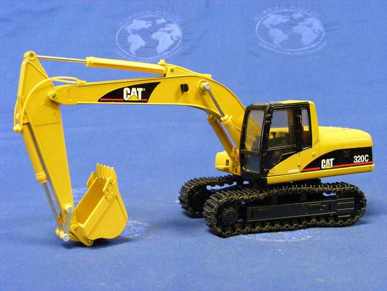 Pode incluir: Um brinquedo escavador Caterpillar 320C amarelo e preto com uma cabine preta e uma ca&ccedil;amba amarela. O escavador est&aacute; em uma esteira preta.