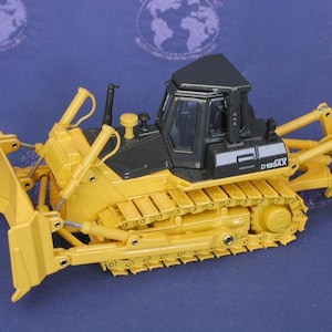 May include: Yellow and black toy bulldozer with a black cab and a yellow blade. The bulldozer has a D155AX label on the side.