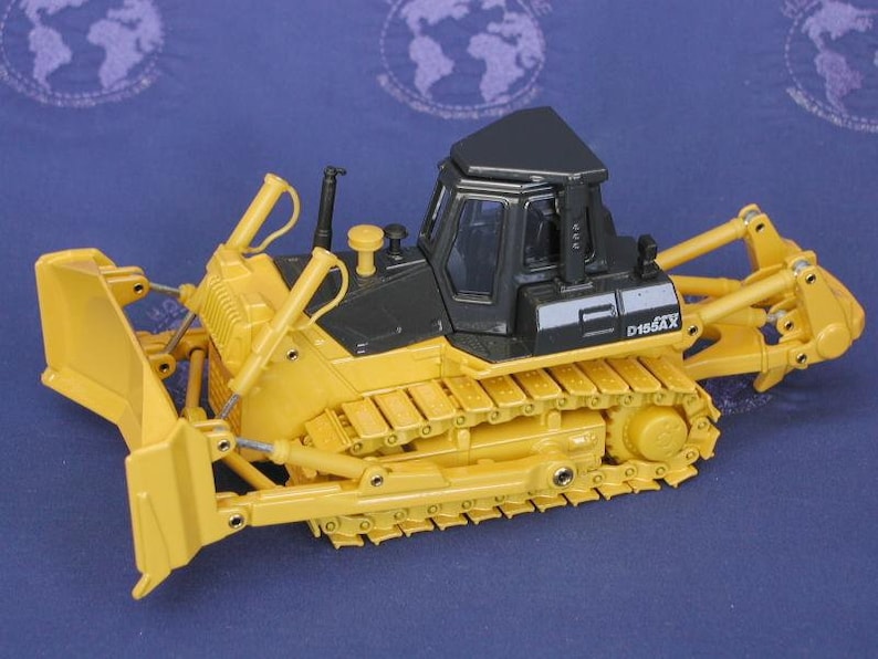 May include: Yellow and black toy bulldozer with a black cab and a yellow blade. The bulldozer has a D155AX label on the side.