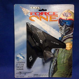 May include: A black die-cast Lockheed F-117A Nighthawk model airplane in its original blister packaging. The card features the Force One logo, an illustration of a pilot in a flight suit, and text identifying the aircraft and the Ertl brand.