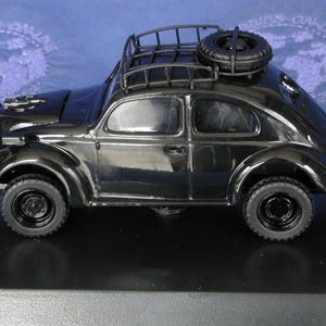May include: Black model car with a roof rack and a spare tyre on the back. The car has a black body and black wheels.