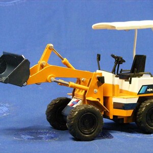May include: A yellow and white toy backhoe with a black bucket. The backhoe has a white canopy and the text "WA30" on the side.