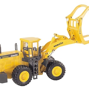 Könnte beinhalten: Ein gelbes Komatsu WA600 Spielzeug-Radlader mit schwarzen Reifen und einem Hubarm. Das Spielzeug hat das Komatsu-Logo und die Modellnummer WA600 auf der Seite. Der Hubarm hat eine Holzgreifer-Aufsatz.